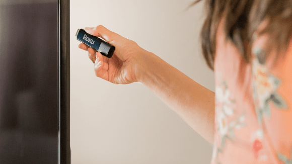 Person plugging their Roku® Streaming Stick®+ into a tv while on vacation