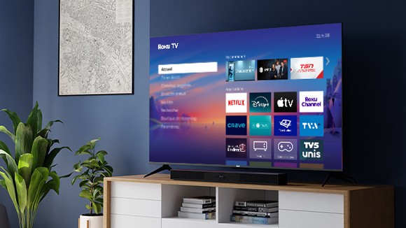 Téléviseur Série Select Roku et barre de son sans fil Roku TV posés sur un meuble bas
